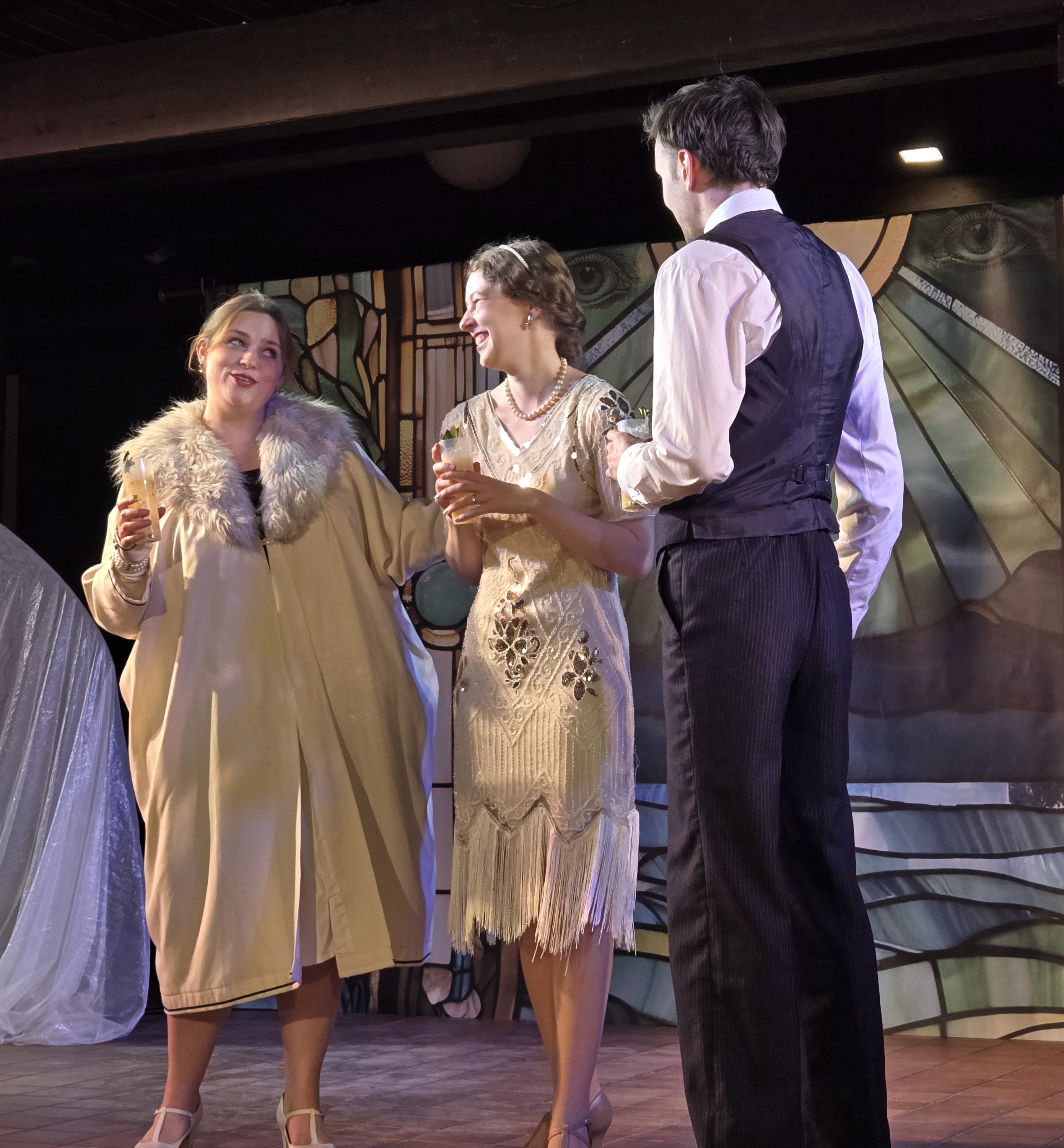 Szene aus „The Great Gatsby“ mit drei Figuren in Kostümen der 1920er Jahre auf der Bühne.